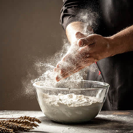 Hands dusting flour over a bowl of flour